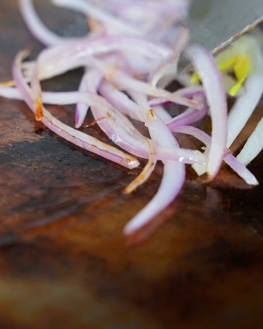 Angus-Rinderbruststreifen und rote Zwiebeln werden zusammen auf einer heißen Grillplatte angebraten.