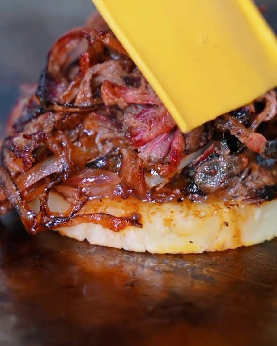 Eine Scheibe gelber Käse schmilzt über dem Stapel aus Rindfleisch, Zwiebeln und Ananas.