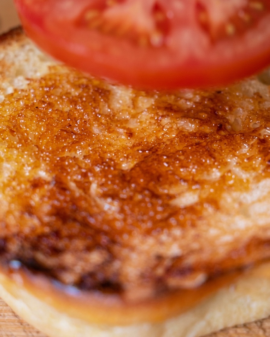 Eine frische Tomatenscheibe wird auf das untere getoastete Burgerbrötchen gelegt.