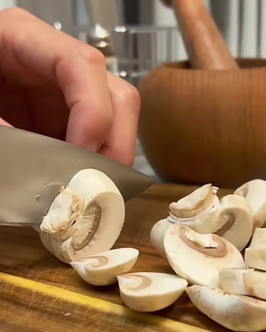 Frische Pilze werden mit einem Messer auf einer Holzoberfläche in Scheiben geschnitten.