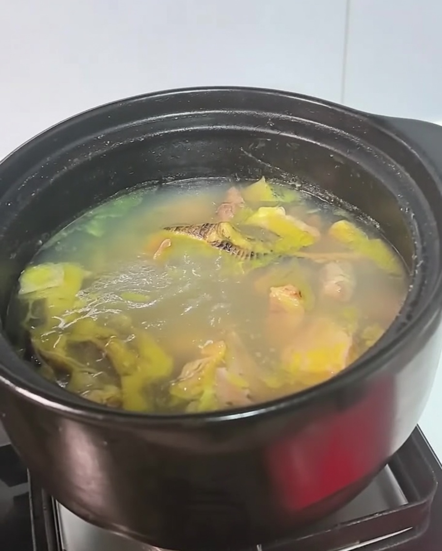 Ein schwarzer Topf mit Hühnersuppe köchelt auf einer Herdplatte.