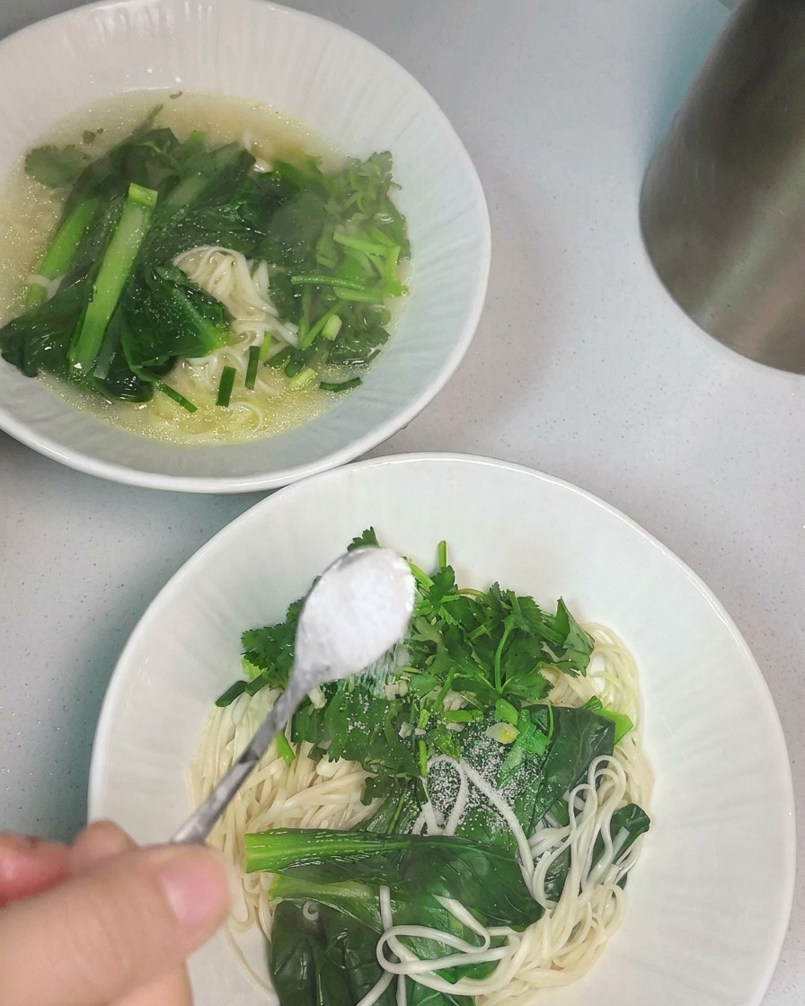 Heiße Hühnersuppe wird mit einer Schöpfkelle über eine Schale mit Nudeln gegossen.