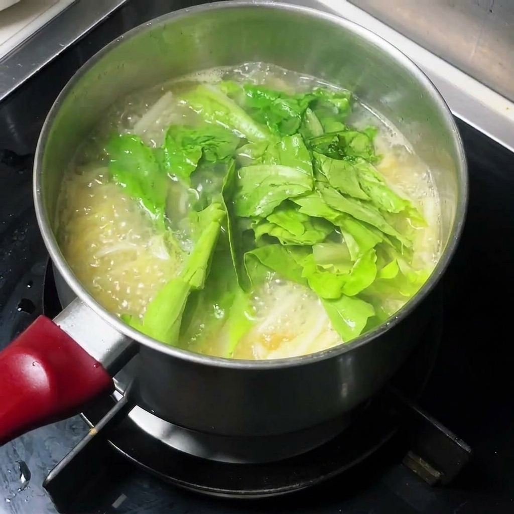 Frisches Blattgemüse wird in den Topf mit Nudelsuppe gegeben.