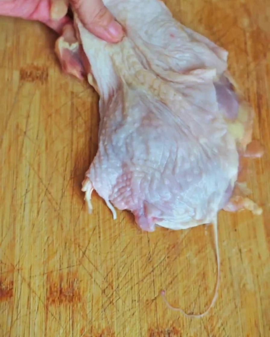 Hähnchenfleisch von der Keule wird auf einem Holzschneidebrett in mundgerechte Stücke geschnitten.