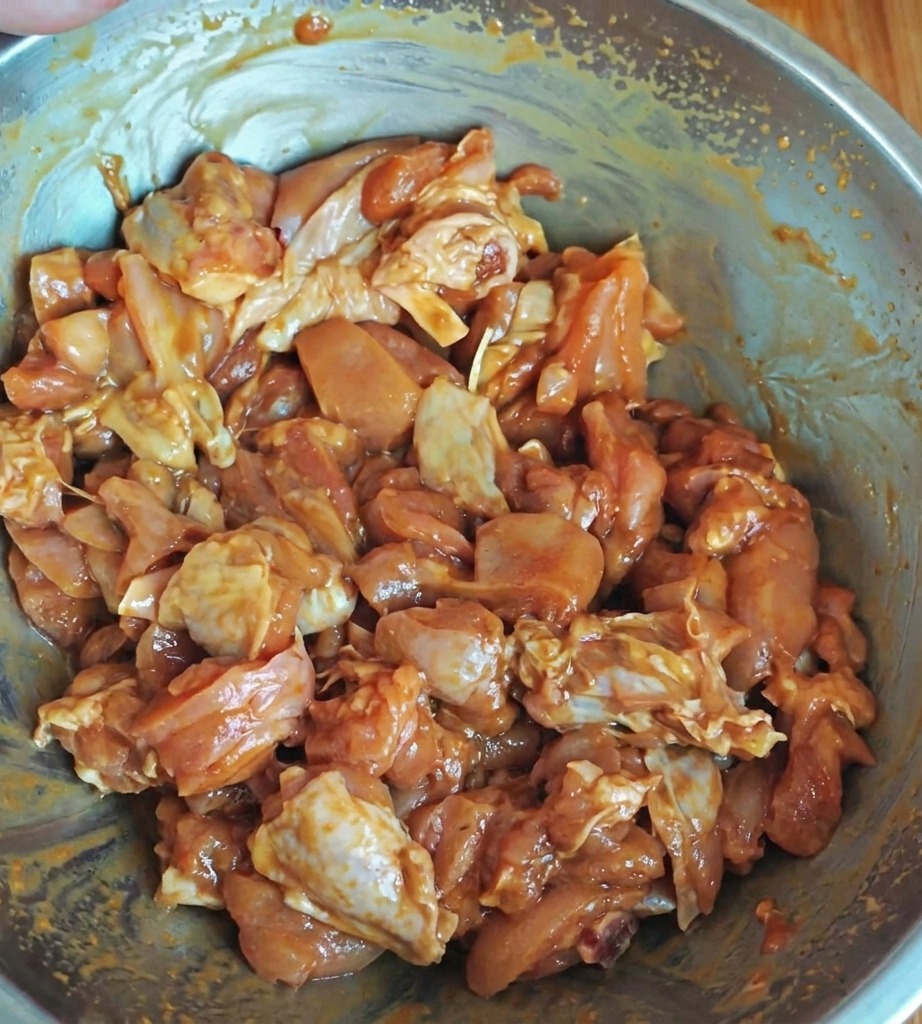 Gewürztes Hähnchenfleisch in einer Metallschüssel, überzogen mit einer glänzenden Marinade.
