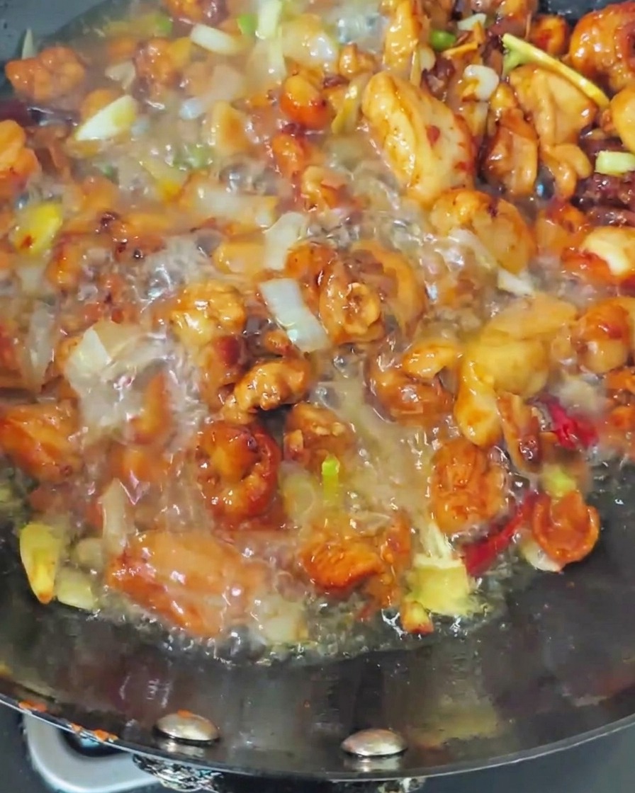 Kochendes Wasser wird über das gebratene Hähnchen im Wok gegossen, es brodelt kräftig.