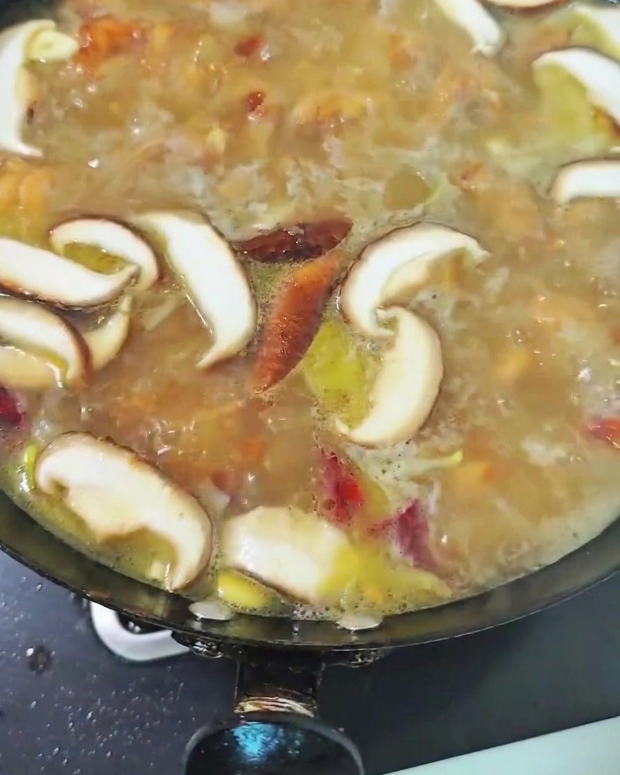 Geschnittene Shiitake-Pilze köcheln in der Hähnchenbrühe im Wok.