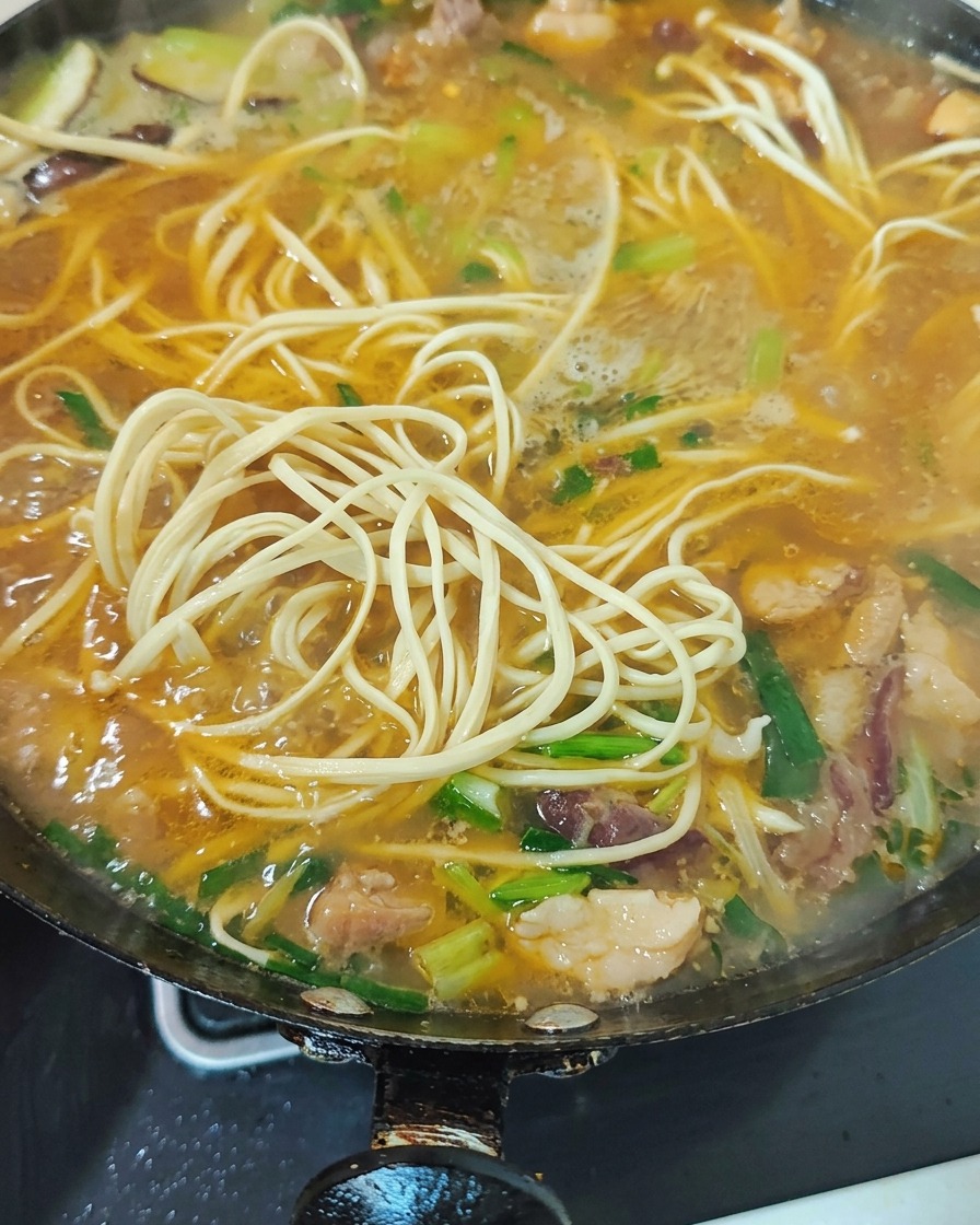 Grünes Gemüse und gehackte Knoblauchsprossen werden in der Suppe untergehoben.