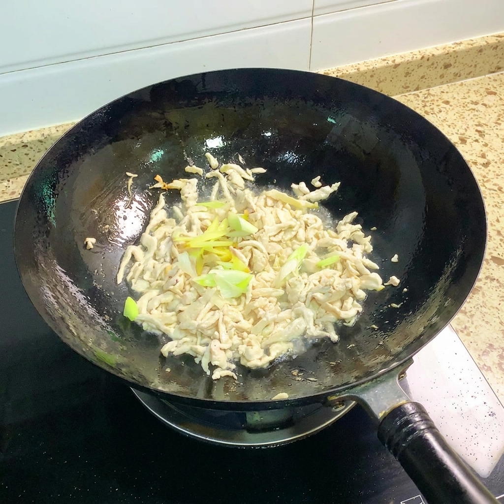 Frühlingszwiebeln und Ingwer werden mit dem gebratenen Hähnchen im Wok geschwenkt.