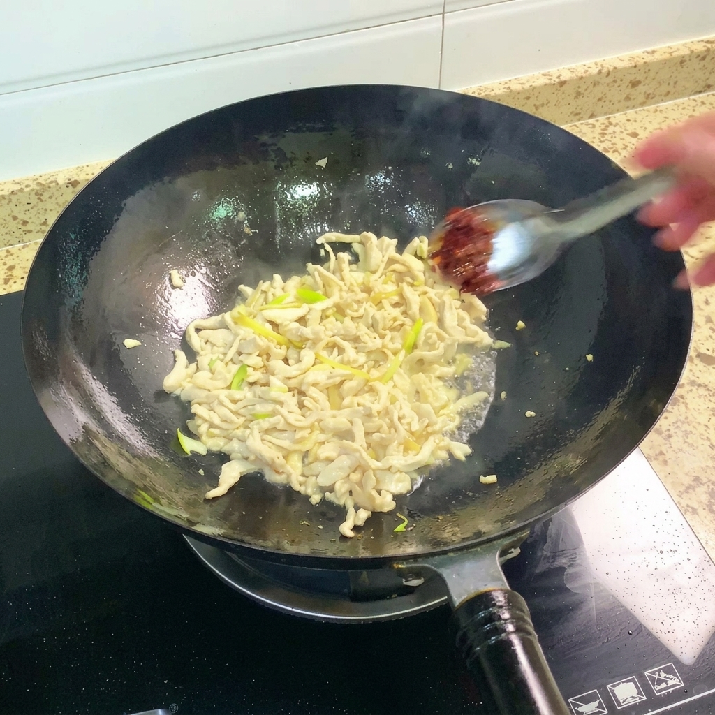 Pixian-Bohnenpaste wird zum Hähnchen im Wok gegeben und untergerührt.