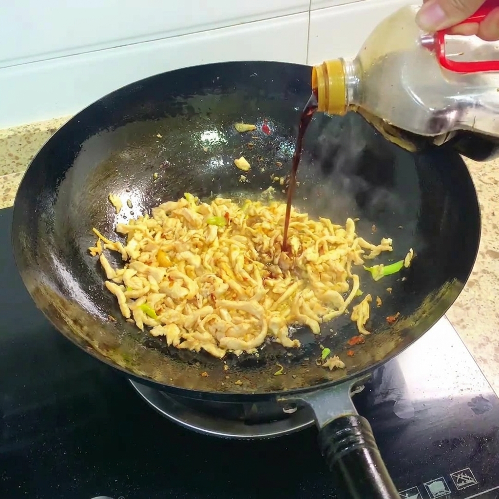 Dunkle Sojasauce wird zum Hähnchen in den Wok gegossen.