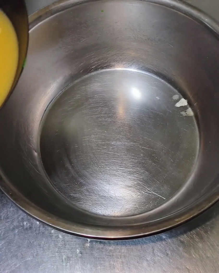 Heiße, gelbliche Brühe wird aus dem Wok in eine große, leere Edelstahlschüssel gegossen.