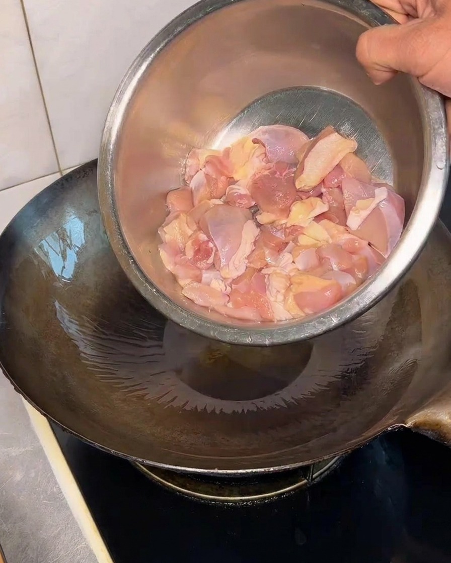 Rohe Hähnchenwürfel werden aus einer Metallschüssel in einen heißen, geölten Wok gegeben.