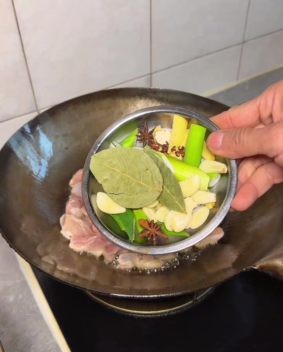 Verschiedene ganze Gewürze werden zum Hähnchen in den Wok gegeben.