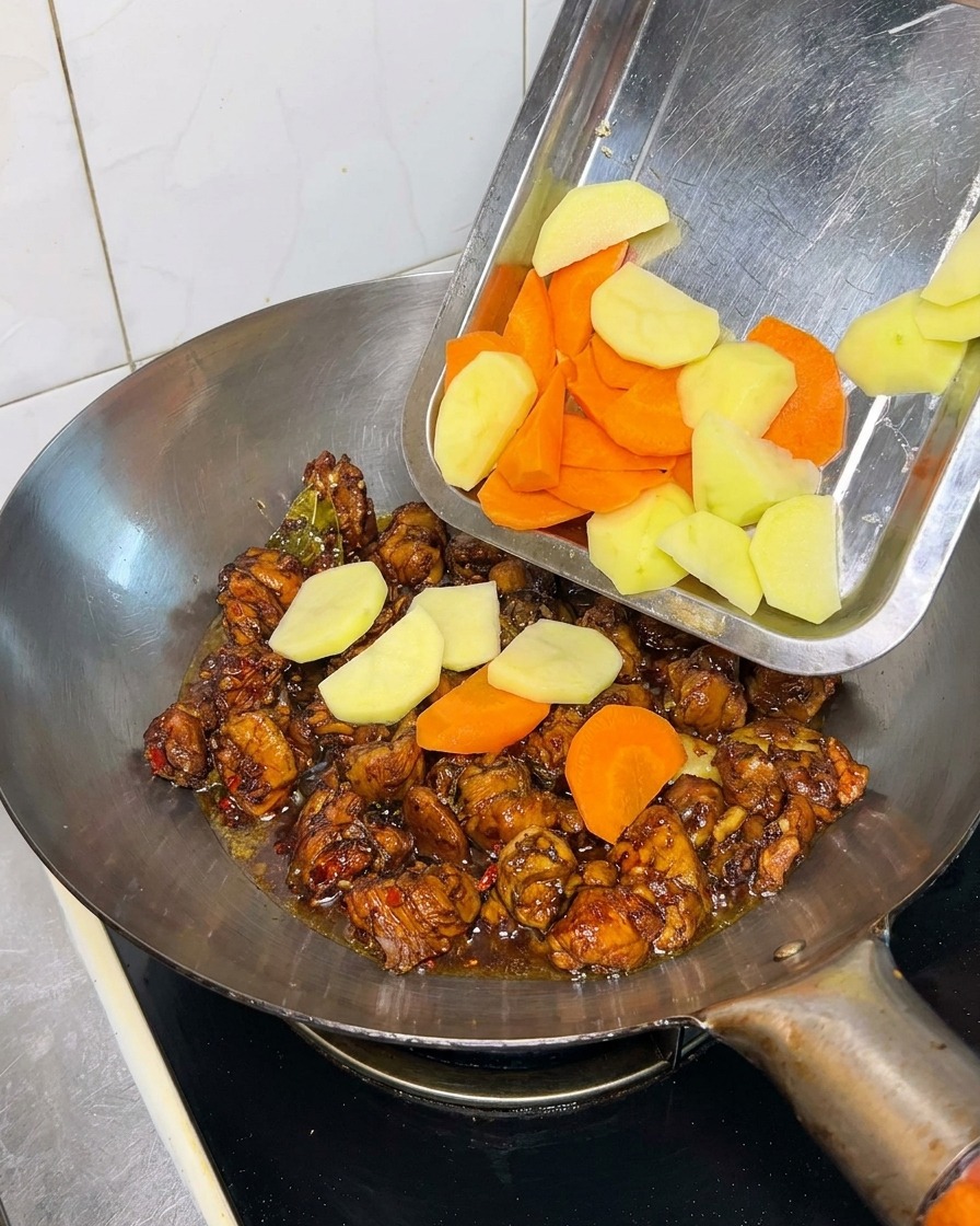Kartoffel- und Möhrenstücke werden in einen Wok zu den Hähnchenteilen gegeben.