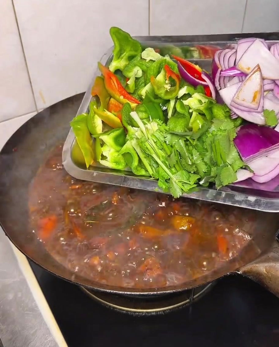 Frische Paprika, Zwiebeln und Koriander werden in den schmorenden Wok gegeben.