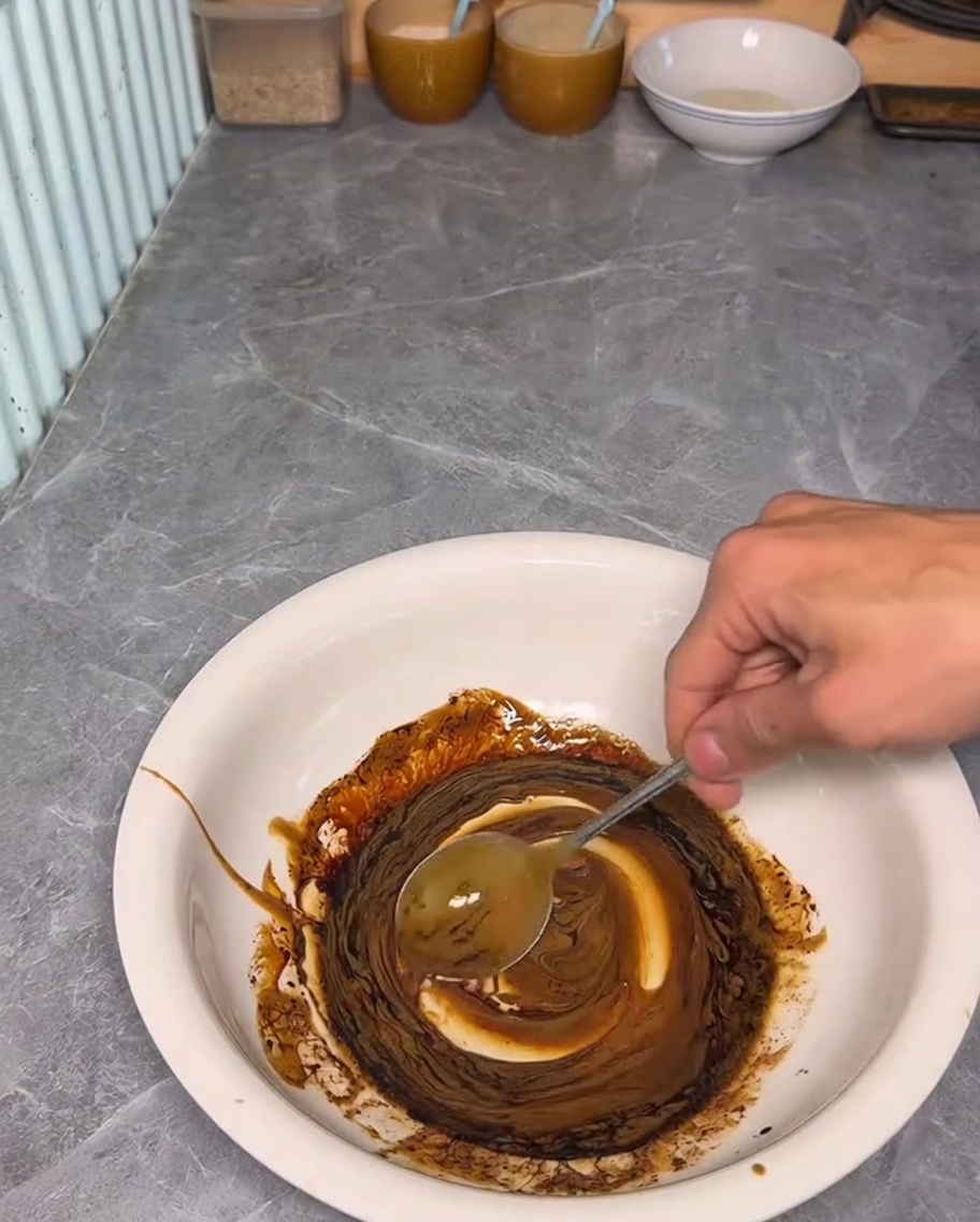 Eine Hand rührt Sesampaste und dunkle Sojasauce in einer weißen Schüssel um.