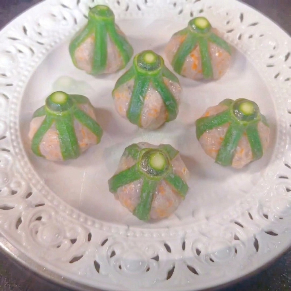 Sechs Okra-Garnelen-Häppchen auf einem weißen Teller in einem Dämpfkorb.