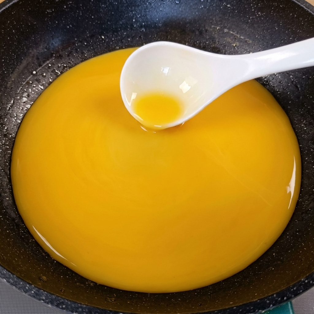 Eine angedickte goldgelbe Sauce wird in einer dunklen Pfanne mit einer weißen Kelle umgerührt.
