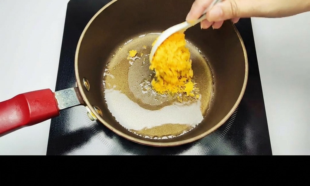 Eine Hand rührt mit einem weißen Löffel zerdrücktes goldenes, gesalzenes Eigelb in einem dunklen Topf an.