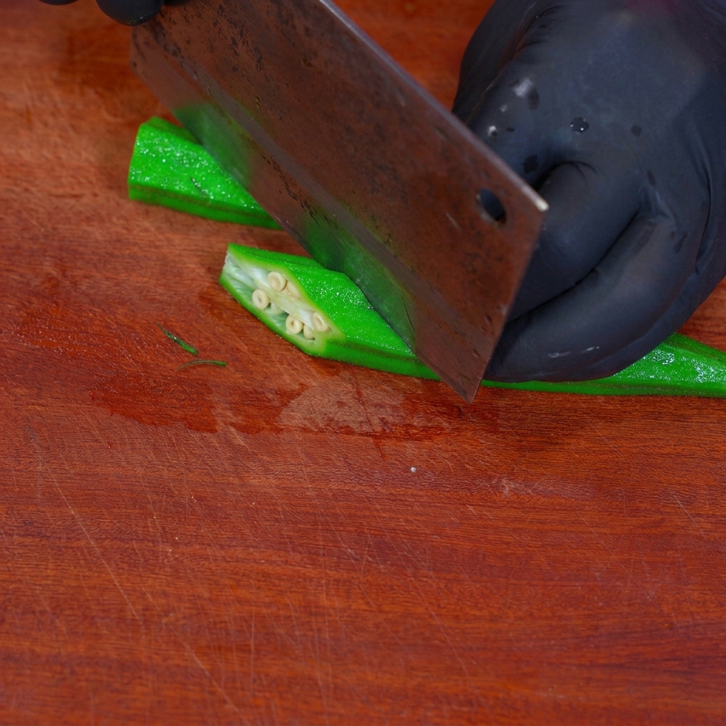 Blanchierte Okra wird auf einem Holzbrett in rautenförmige Stücke geschnitten.