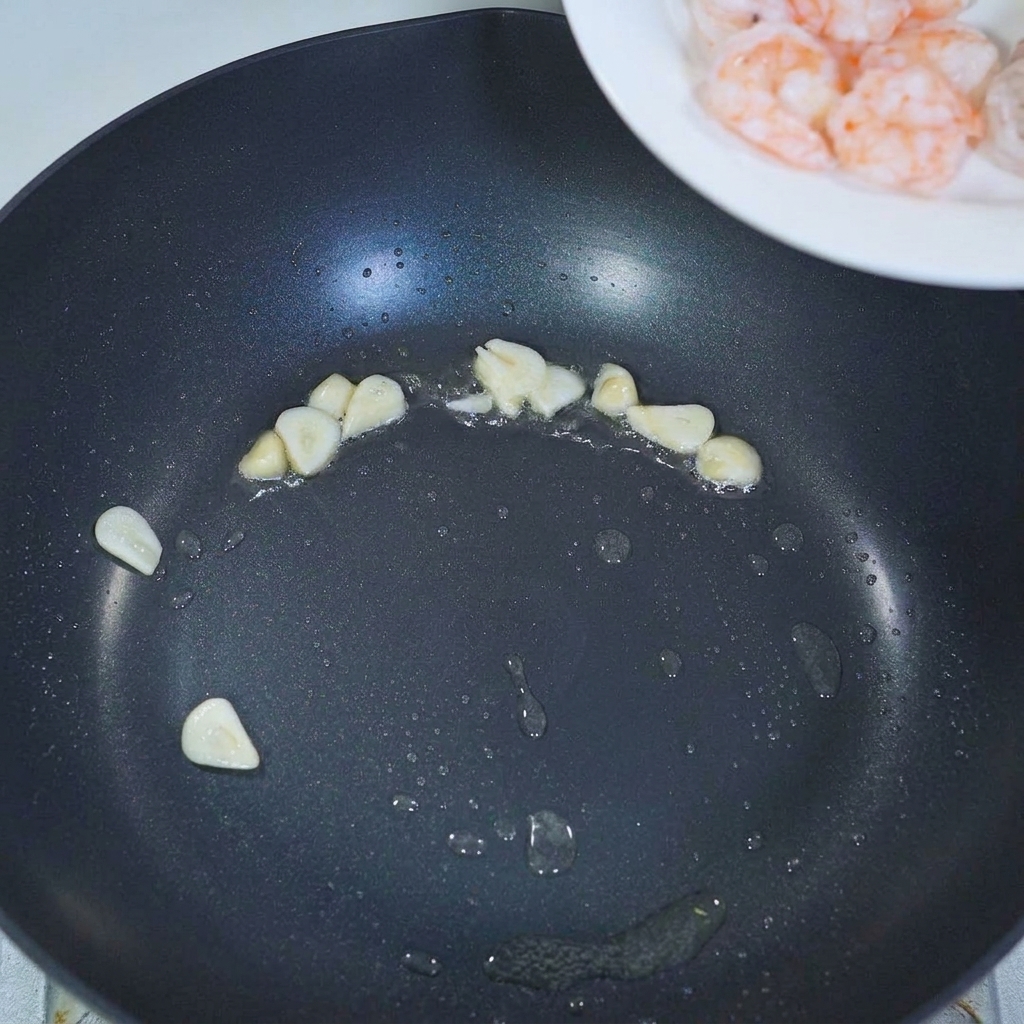 Vorgekochte Garnelen werden in eine Pfanne zu den angedünsteten Knoblauchscheiben gegeben.