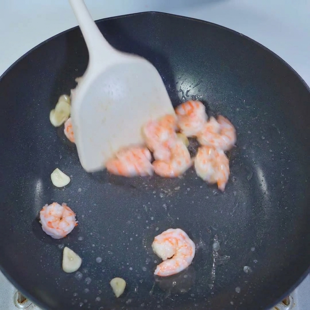 Okrasücke werden in einer Pfanne zusammen mit Garnelen und Knoblauch mit einem weißen Spatel geschwenkt.