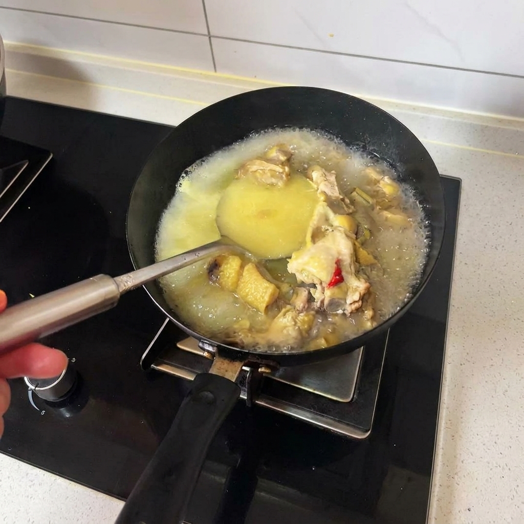 Eine Schöpfkelle rührt heiße goldene Hühnerbrühe und gekochte Hähnchenstücke in einem schwarzen Wok um.