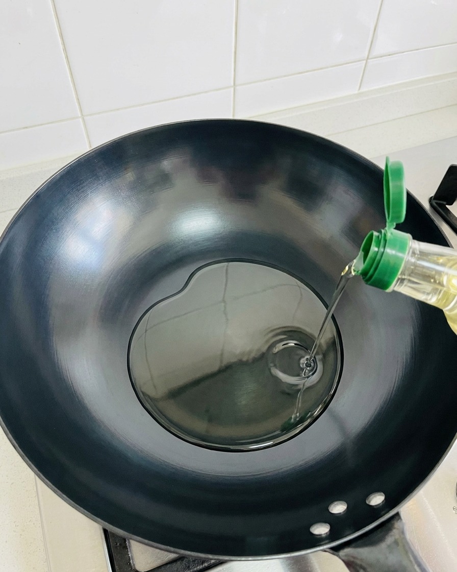 Olivenöl fließt in einen heißen, leeren Wok.