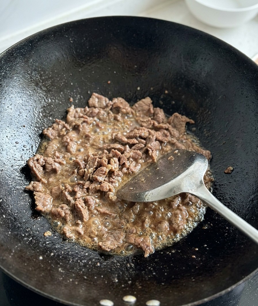 Gewürfelte Tomaten werden zum gebräunten Fleisch in den Wok gegeben.