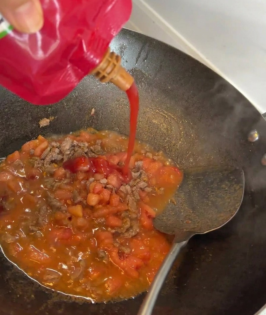 Tomatenmark wird in die Pfanne zu Fleisch und Tomaten gegeben.