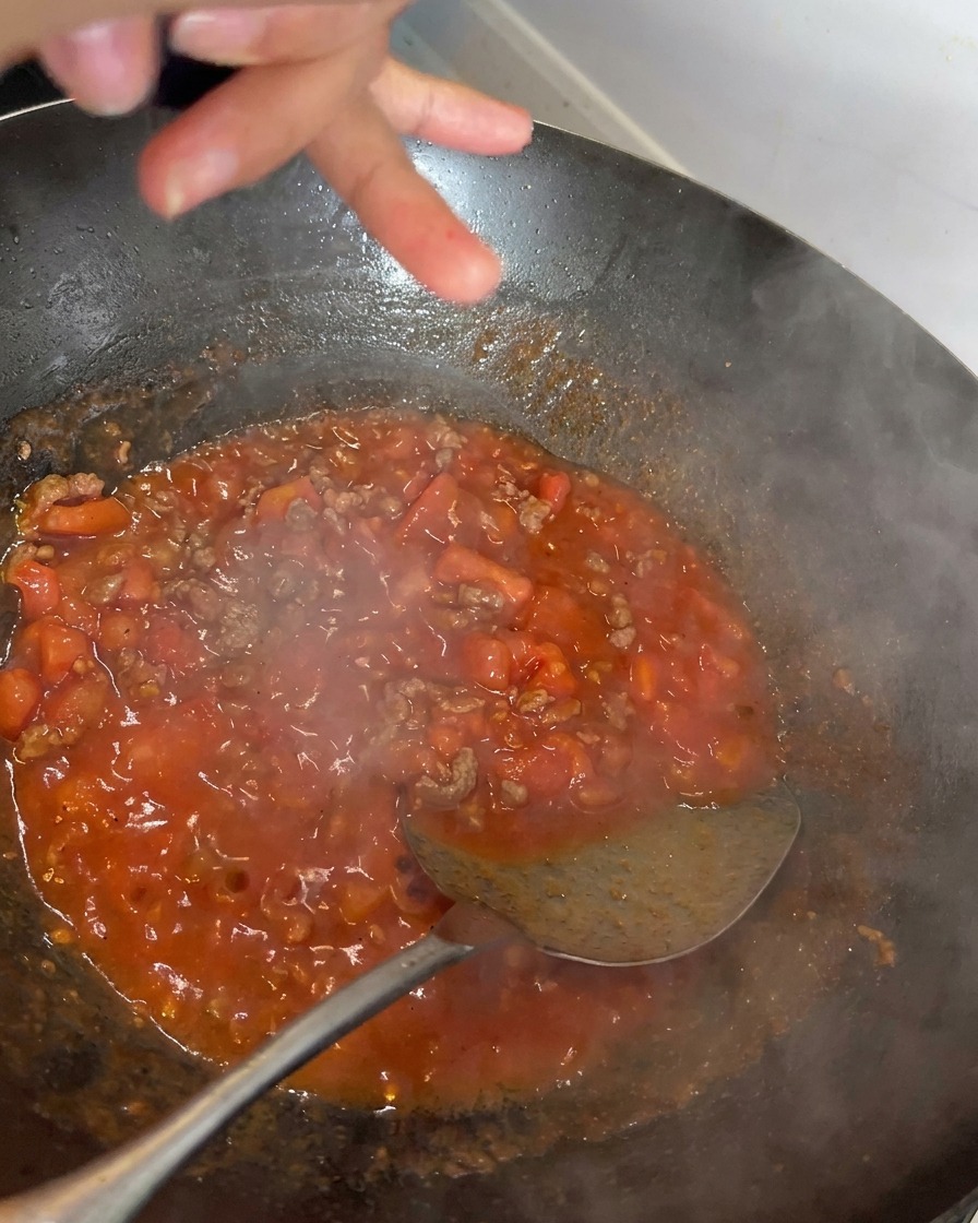 Schwarzer Pfeffer wird frisch über die köchelnde Tomaten-Rindfleisch-Soße gemahlen.