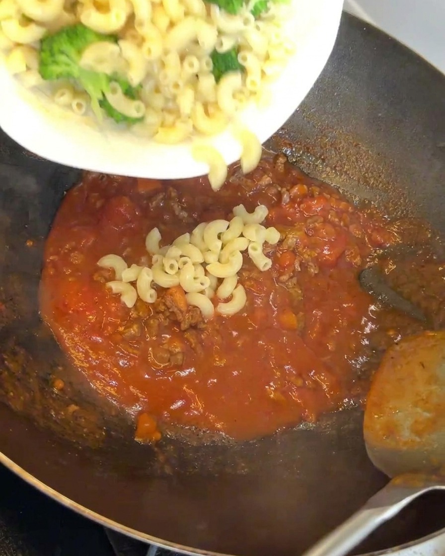 Nudeln und Brokkoli werden unter die Fleischsoße im Wok gemischt.