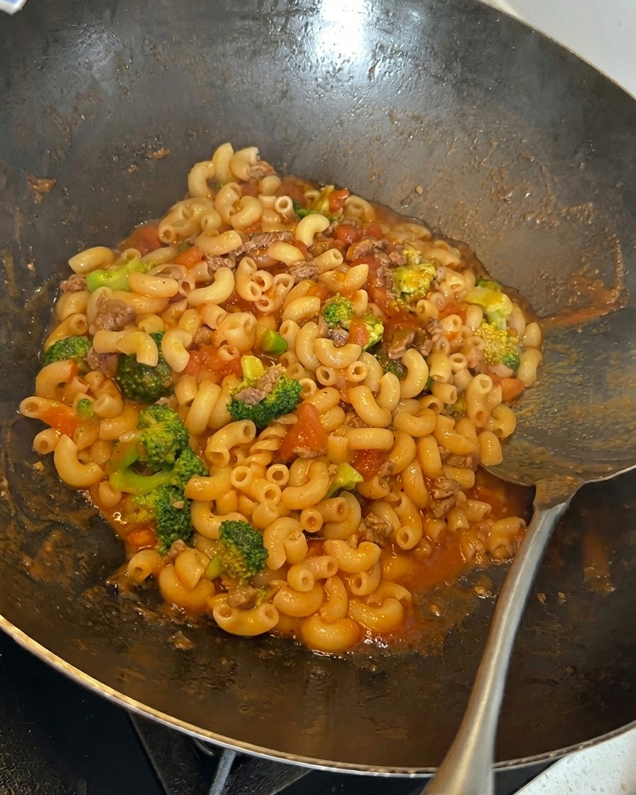 Geriebener Käse wird über die Nudelmischung im Wok gestreut.