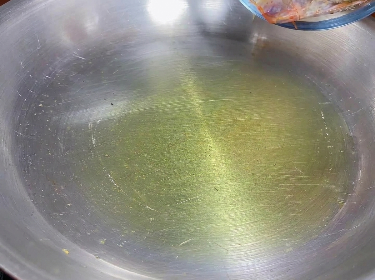 Garnelenköpfe braten in Olivenöl in einer Edelstahlpfanne.