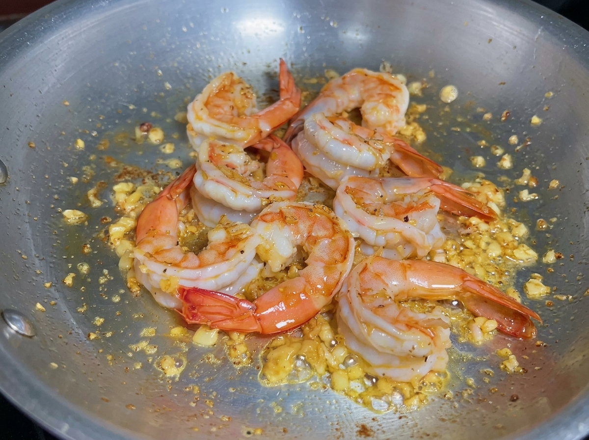 Flüssigkeit wird in eine Pfanne mit gekochten Garnelen gegossen, um abzulöschen und Aromen zu sammeln.