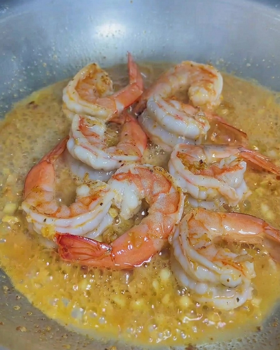 Sahne wird in eine Pfanne mit gekochten Garnelen und gehacktem Knoblauch gegossen.
