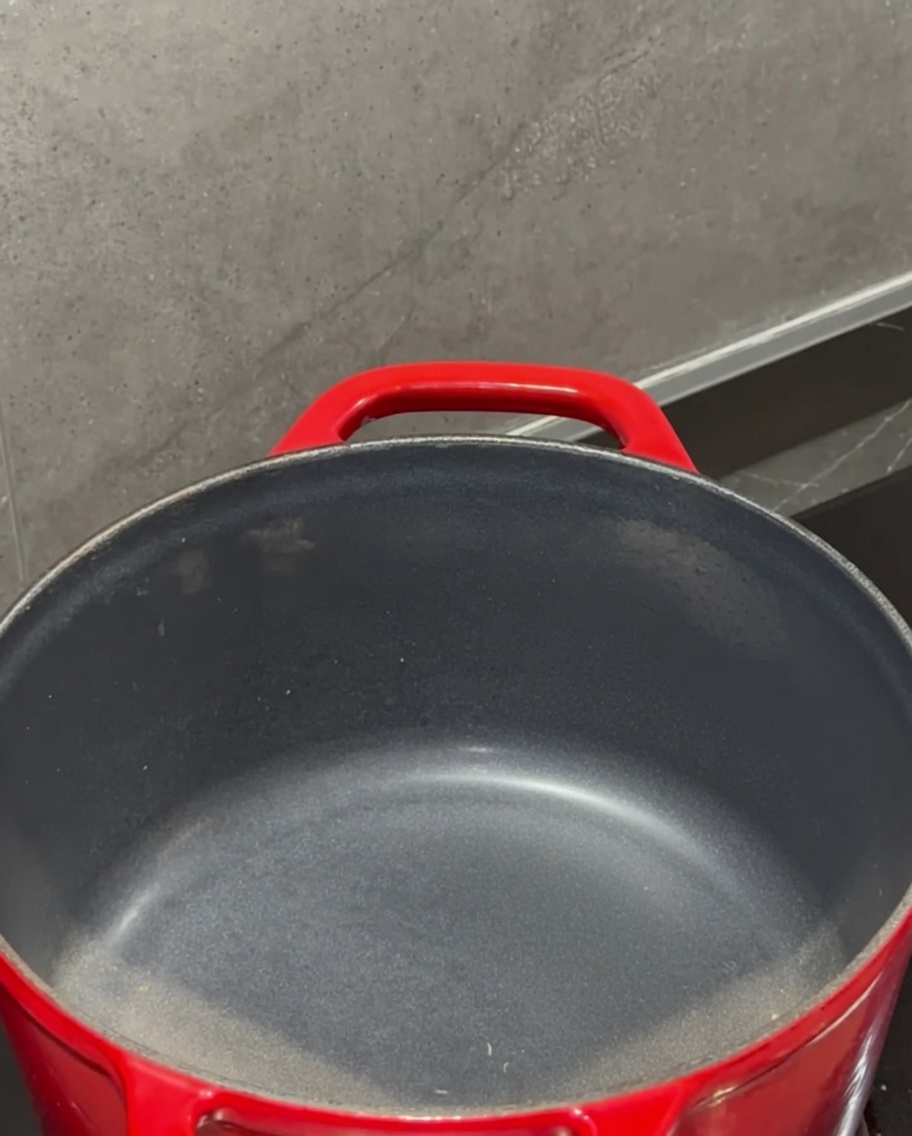 Ein Stück Butter schmilzt in einem roten Topf auf dem Herd.