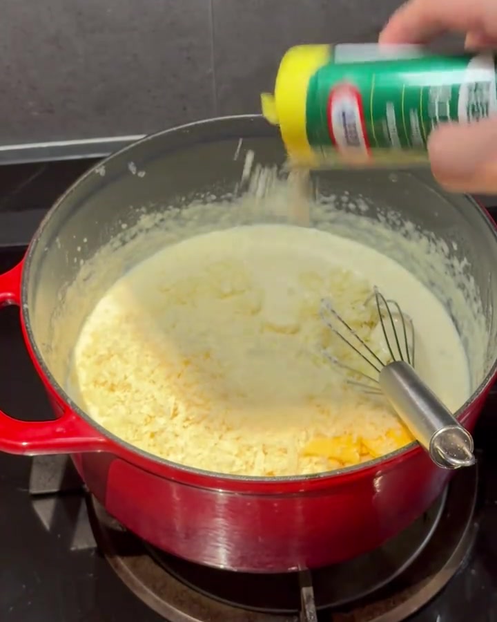 Käsepulver wird in eine cremige Sauce in einem roten Topf eingerührt.