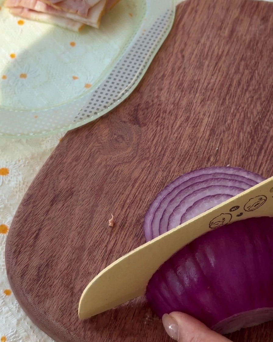 Dünn geschnittene rote Zwiebelstreifen auf einem Holzbrett.
