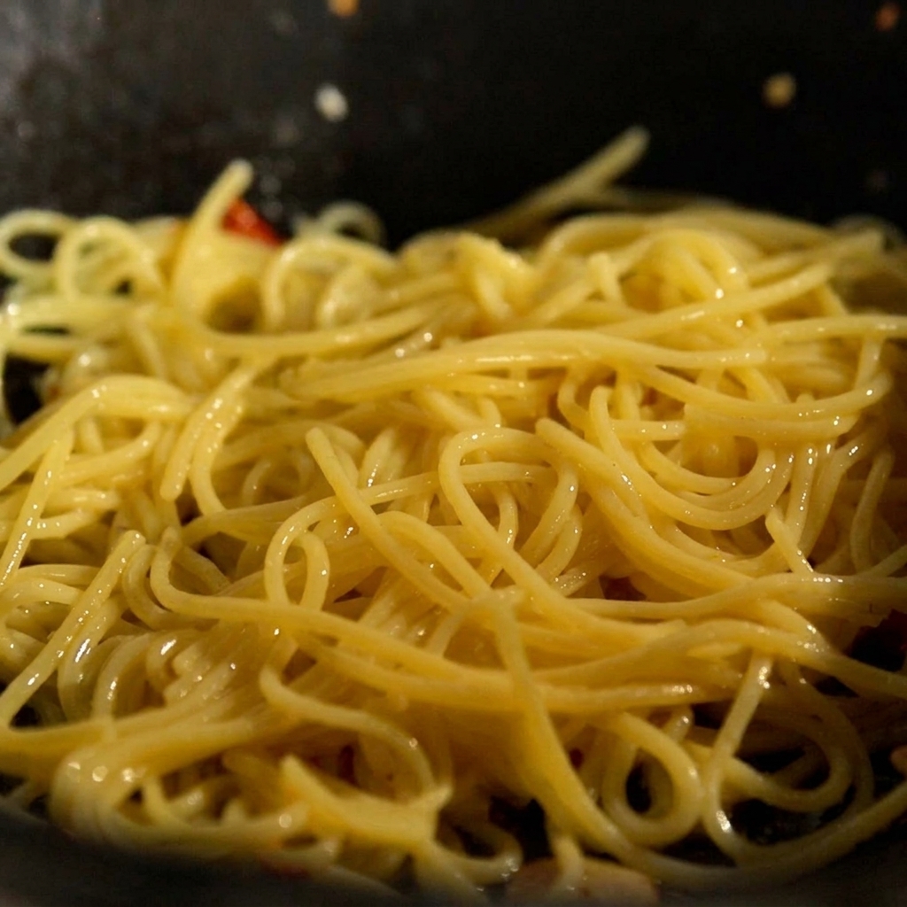 Gekochte Nudeln und ein Stück Butter werden in die Pfanne zu Knoblauch und Chili gegeben.
