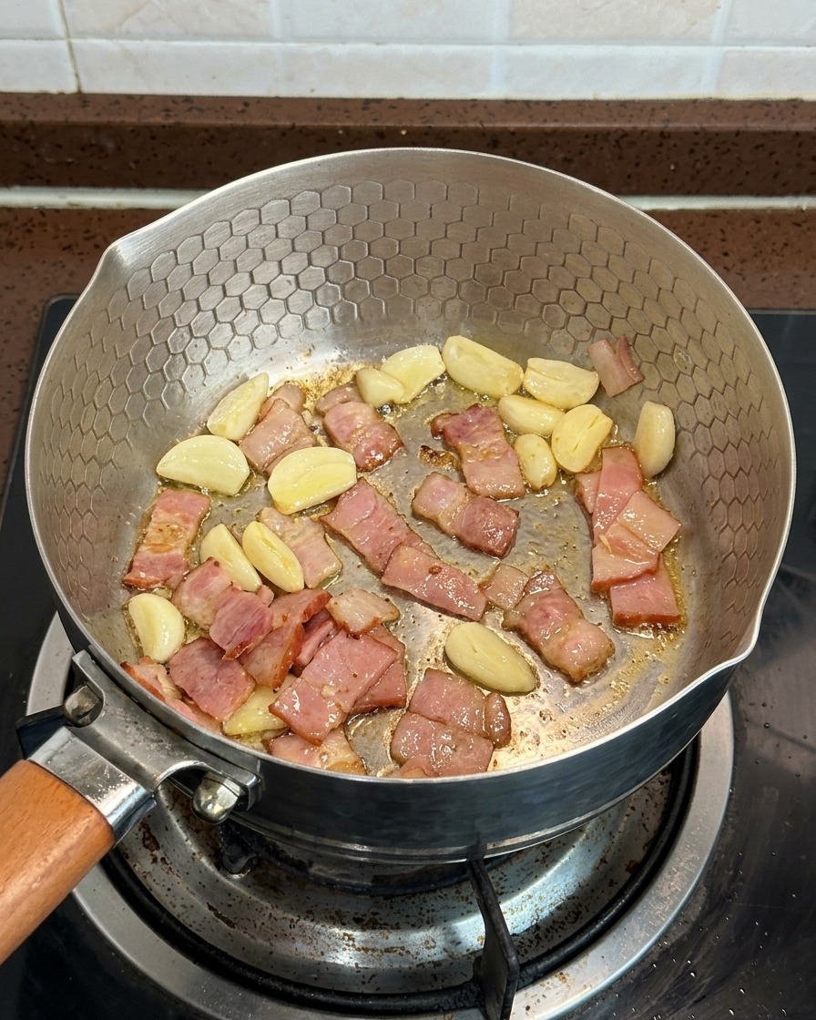 Geschnittene Pilze, Speckwürfel und Knoblauchscheiben, die zusammen in einer Pfanne garen.