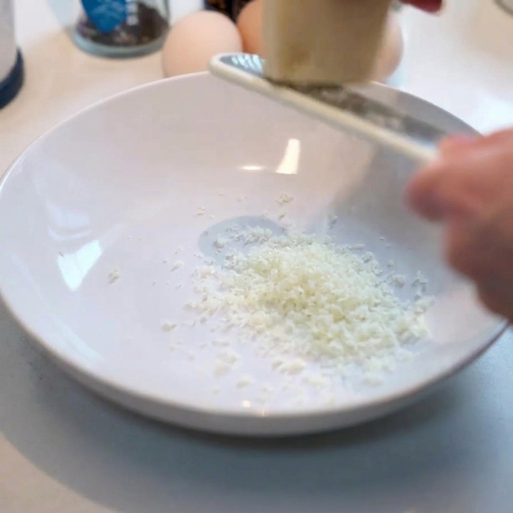 Frischer Parmesan wird in eine saubere weiße Schüssel gerieben.