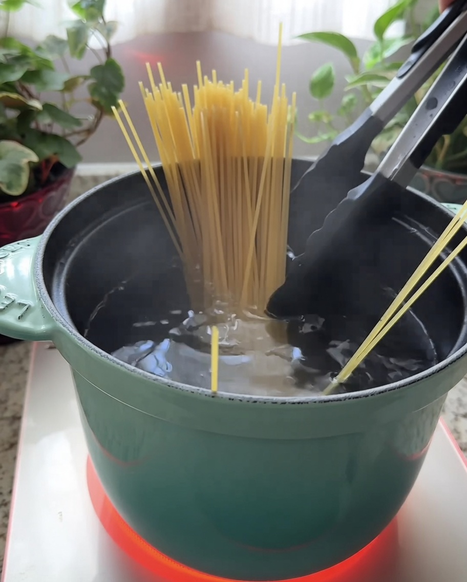 Trockene Spaghetti werden in einen blaugrünen Topf mit kochendem Wasser getaucht.