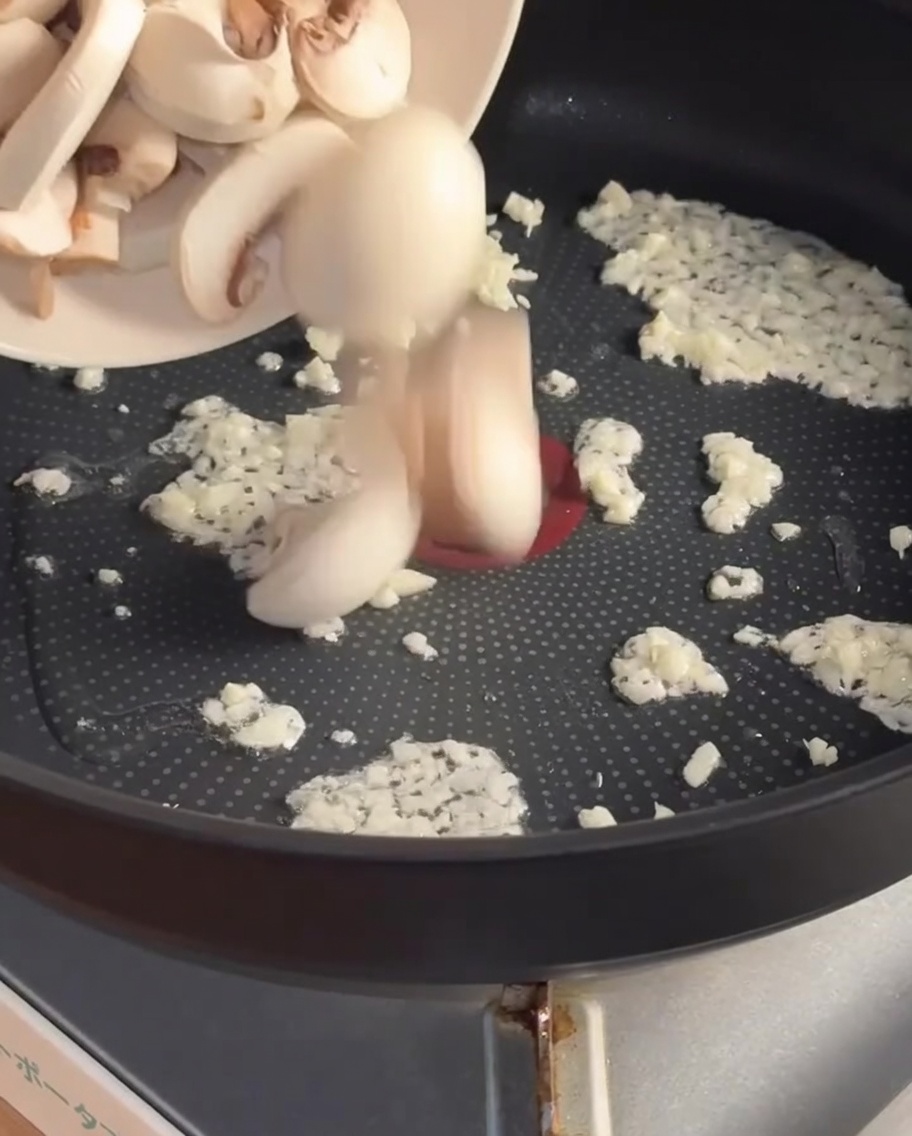 Geschnittene Pilze werden zum angebratenen Knoblauch in die Pfanne gegeben.