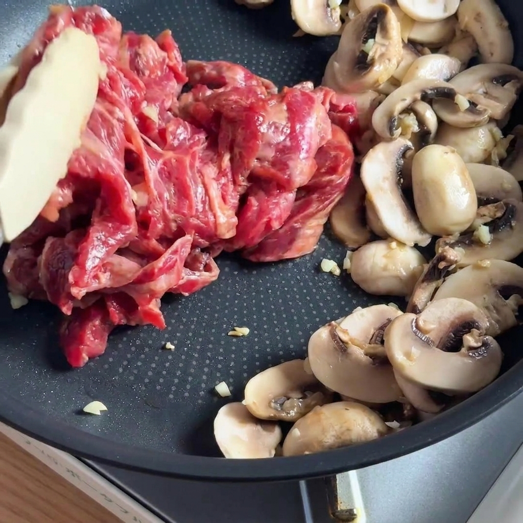 Marinierte Rinderstreifen werden mit Pilzen in der Pfanne angebraten.