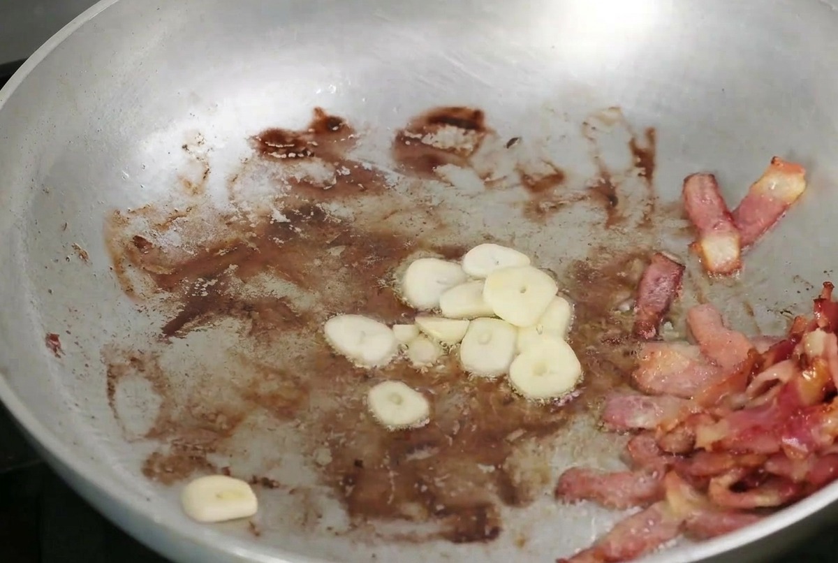 Gehackter Knoblauch und Pilze in der Pfanne neben dem Speck.