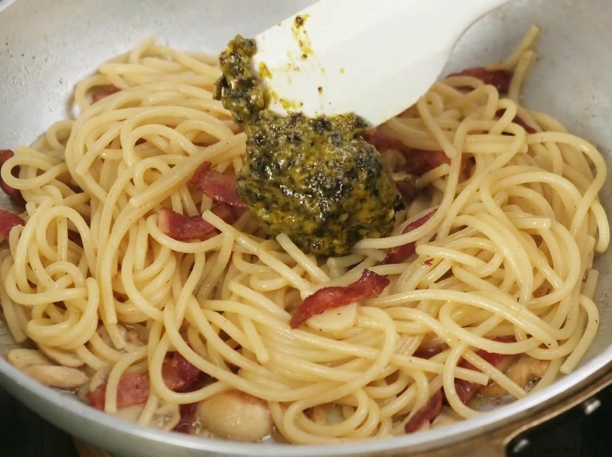 Dunkle Trüffelsauce wird mit einem Spatel unter die Pasta gemischt.