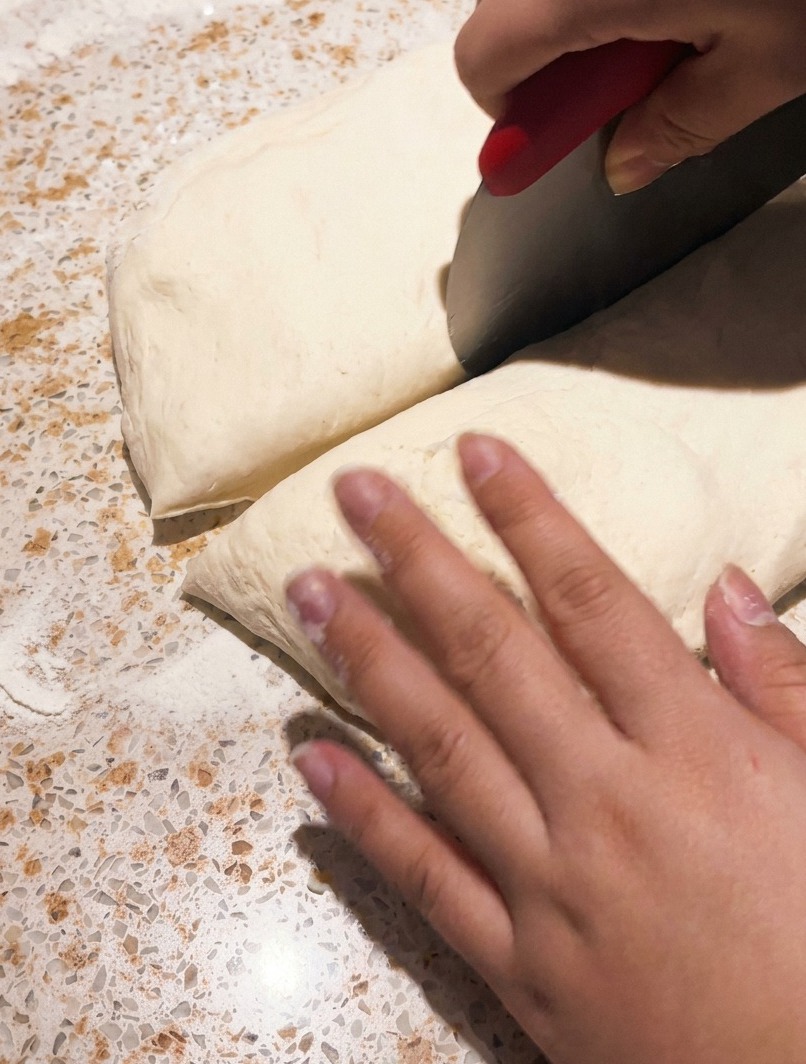 Ein Teigschaber teilt Pizzateig auf einer Arbeitsfläche.