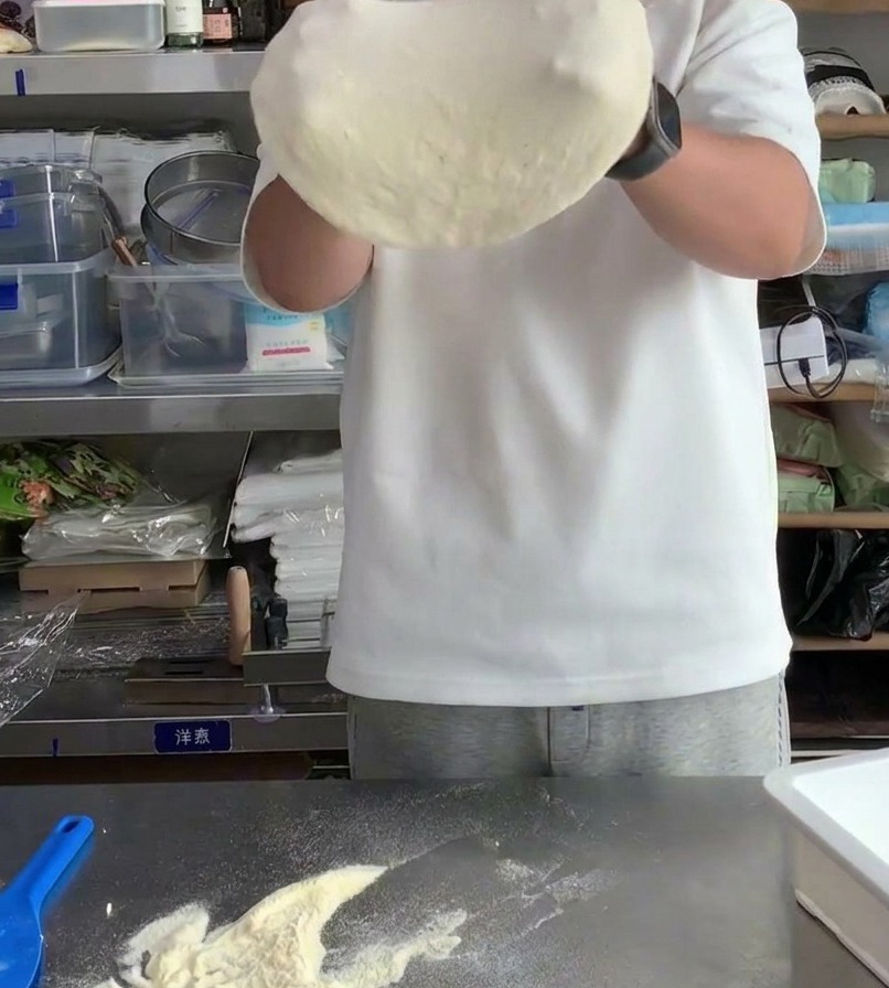 Pizzateig wird über die Knöchel gezogen, um den Durchmesser zu vergrößern und die Mitte auszudünnen.